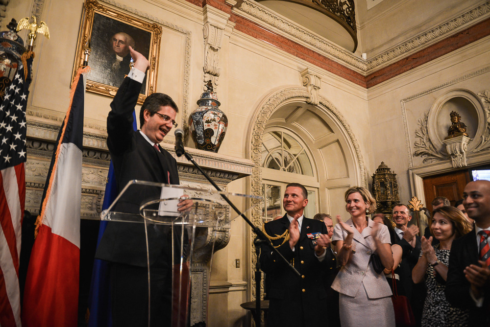 French Ambassador François Delattre says goodbye to a warm-hearted party of well-wishers at his goodbye party in Washington, DC on July 10, with French Defense Attache Brigadier General Bruno Caïtucoli (center) and the Ambassador's wife Sophie (pink) standing by. Guests cheered as the Ambassador gave a light-hearted speech celebrating strong relations between the US and France before bidding adieu (Kate Warren for The Washington Post).
